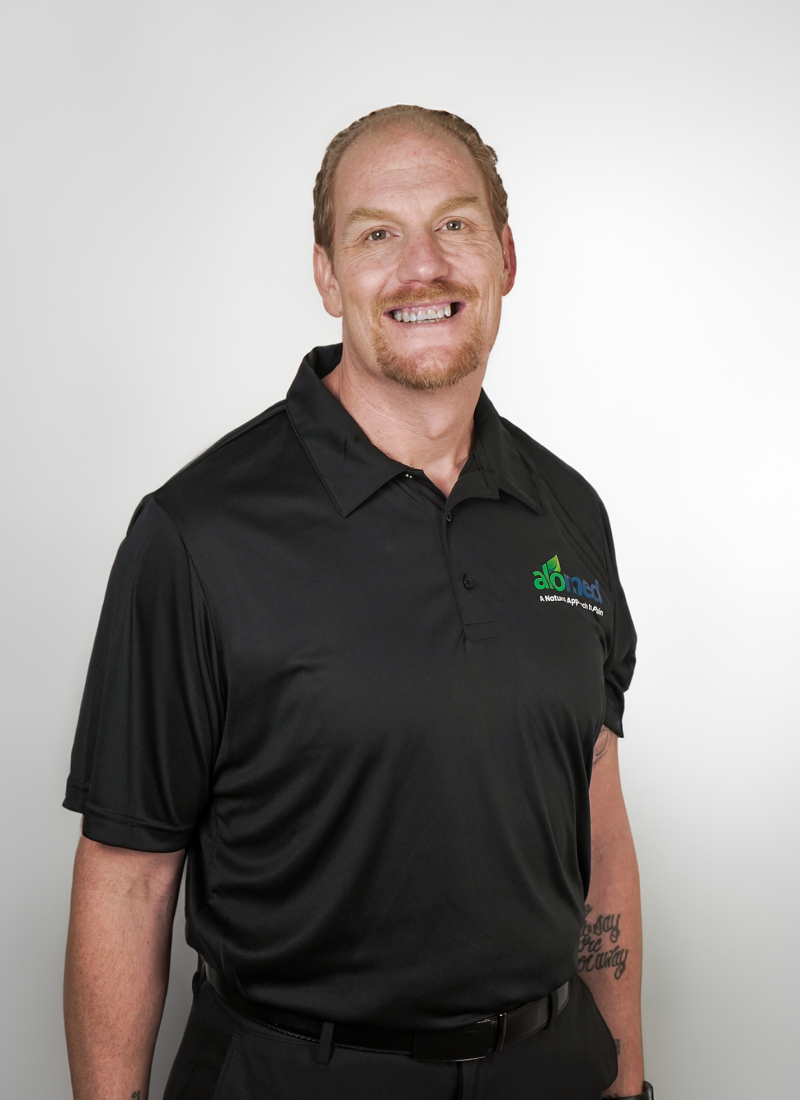 Nate Rasner smiling while wearing a black Alomed-branded polo shirt.
